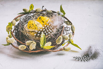Holiday still life with decorative quail eggs in a brown nest among feathers. Easter decor with selective focus