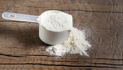 plastic measuring scoop of white powder (whey protein) against grunge wood background