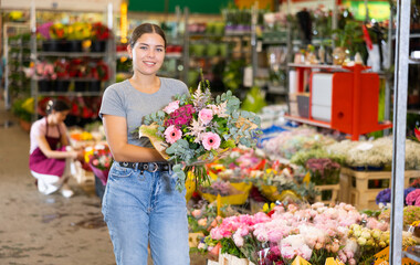 Smiling interested young girl buying bouquet of colorful fresh flowers at market