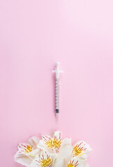 White flowers and medical syringe on pink background. Minimal concept of beauty injections....