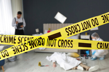 Yellow tapes blocking way to crime scene. Investigator and criminologist working in room