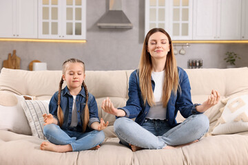 Mother with daughter meditating on sofa at home. Harmony and zen