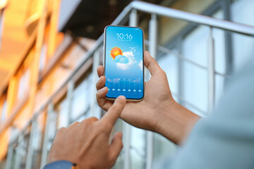 Man checking weather using app on smartphone outdoors, closeup. Data and illustration of sun with...