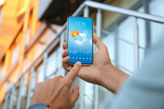 Man checking weather using app on smartphone outdoors, closeup. Data and illustration of sun with cloud on screen