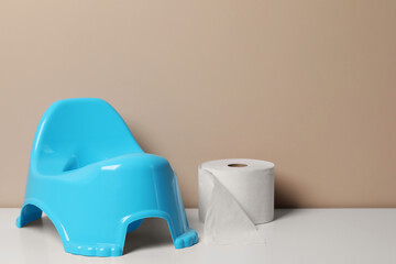 Light blue baby potty and toilet paper on white table near brown wall, space for text