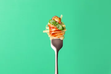 Poster Tasty pasta with tomato sauce and basil on fork against green background © New Africa