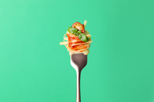 Tasty pasta with tomato sauce and basil on fork against green background