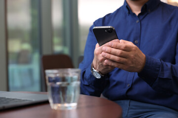 Man sending message via smartphone at table indoors, closeup