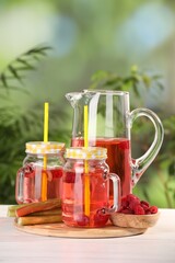 Tasty rhubarb cocktail with raspberry and stalks on white wooden table outdoors