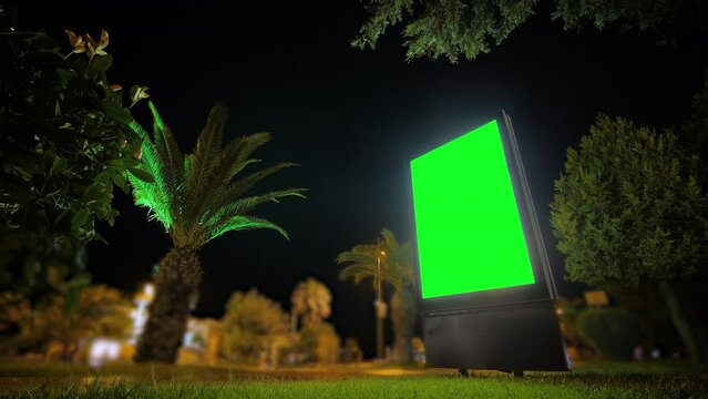 Timelapse: blank vertical street green billboard poster or advertising pillar, fast moving people at night in Batumi - blurred background. Time lapse, green screen, copyspace, chroma key concept