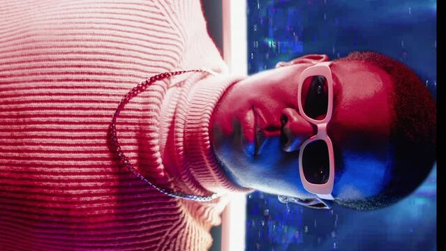 Vertical video. Cyber people. Digital art. Synthwave party. Red blue neon light portrait of confident guy in sunglasses on glitch static noise motion color smoke background.