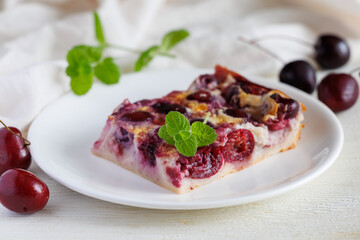 A slice of homemade yummy clafoutis with cherry on a white plate. Traditional french cherry pie