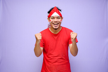Excited Indonesian man celebrate indonesian independence day on 17 August, wearing red shirt. isolated on purple background. copyspace