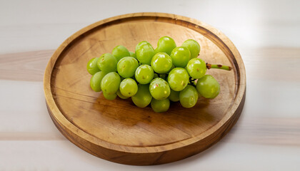 A small bunch of green grapes on a small round wooden serving board