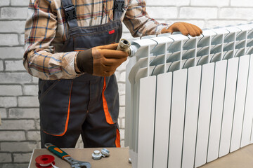 Man in work overalls repairing or installing heating radiator in room.