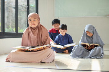 Smiling young Muslim Asian teen girl looking at camera while sitting on mosque floor after reading...