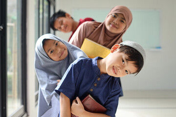 Happy smiling Muslim little kids holding holy book of Quran and standing in a row one after another near window. Diversity and friendship concept