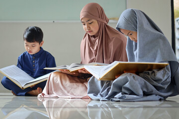 Group of muslim children sitting on the floor inside mosque and reading Quran together during...