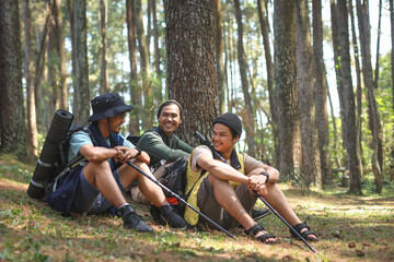 Group of hiker male friends sits resting on grass among the pines mountain forest. Travel, hiking, backpacking, tourism and people concept
