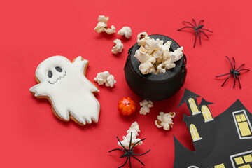 Bowl with tasty popcorn, cookie, spiders and paper house on red background, closeup. Halloween celebration