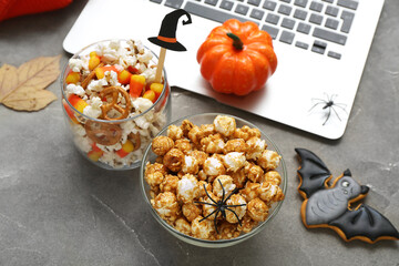 Composition with tasty popcorn, cookie and laptop on grey background, closeup. Halloween celebration