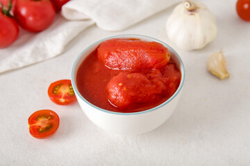Bowl of canned tomatoes and garlic on light background