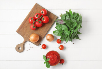 Composition with canned, fresh tomatoes, onion and basil on light wooden background