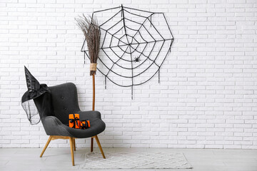 Armchair with gift boxes, broom, hat and web hanging on light brick wall in room