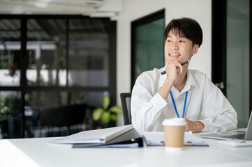 A smart and thoughtful Asian male office worker is looking out the window and daydreaming