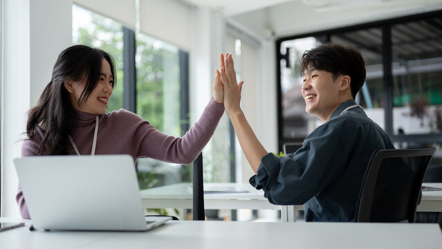 Two cheerful Asian workers give high fives to each other to celebrate a successful project
