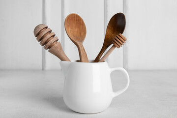 Ceramic pitcher with wooden kitchen tools on light background