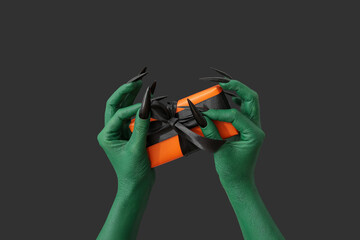 Naklejka premium Green hands of witch with gift box on dark background. Halloween celebration