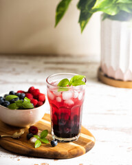 The glass of iced tea with berries on the wooden table.