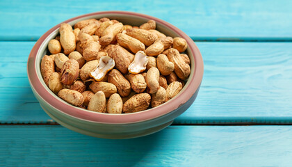 Bowl of fried peanuts with nutshell on turquoise wooden background