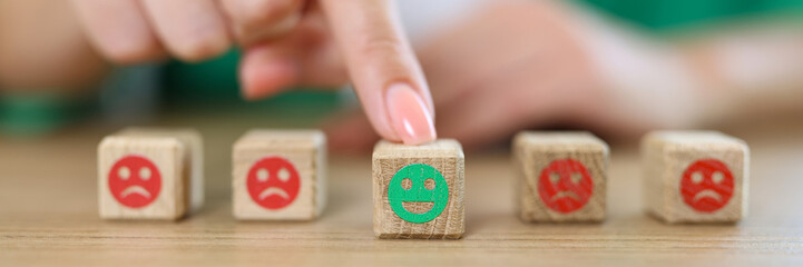 Woman's hand chooses happy emoji from wooden cubes with sad and happy emoji. .
