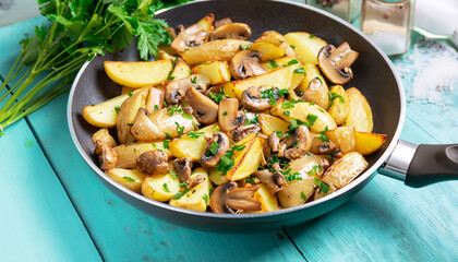 Fried potatoes with mushrooms, onions and parsley served in a frying pan with turquoise wooden...