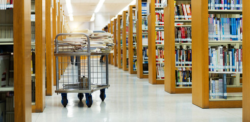 Interior of library with book shelves and books in cart © xy