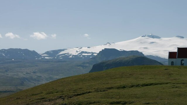 Ingjaldsh&oacute;lskirkja church on green hill, snowy glacier in background, pan right