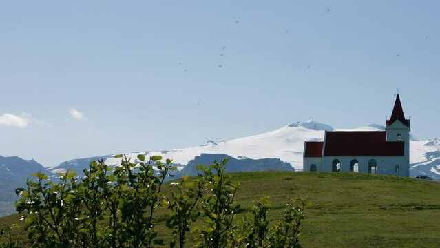Stone church Ingjaldsholskirkja on green hill, Sn&aelig;fellsj&ouml;kull glacier behind