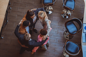 Top view of team of successful colleagues laughing and hugging while standing in circle in coworking