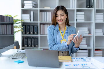 Smiling happy asian businesswoman sitting with laptop computer taking notes in office.