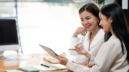 Happy young entrepreneurs smiling while working together in a modern workspace. Two young businesspeople sitting together at a table.