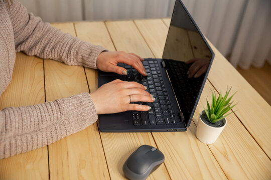 Young woman working on laptop at home. Female hands typing on pc keyboard. Teenager making an Internet video call with remote friends. Hands of a female freelancer, working behind the table at home.