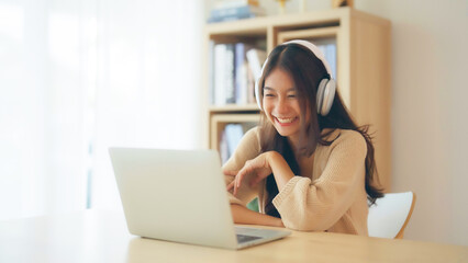 Young asian woman wearing headset while working on computer laptop at house. Work at home, Video conference, Video call, Student learning online class - obrazy, fototapety, plakaty