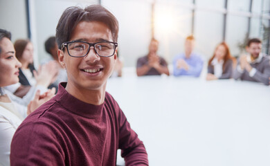 Young handsome businessman in glasses posing for the camera against the background of his colleagues