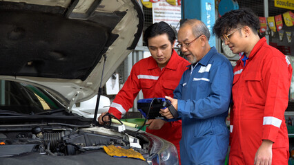 senior asian car mechanic manager training apprentice to checking car engine by Diagnostics Software repair in garage . old asia Auto mechanic teaching trainee or assistant on the repair shop . - obrazy, fototapety, plakaty