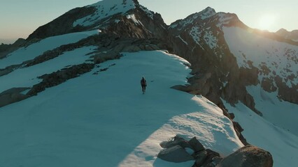Drone shot from behind of a female mountaineer hiking across a scenic snowfield at sunrise in the mountains of South Tyrol, Italy.
