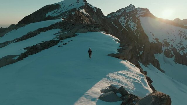 Drone shot from behind of a female mountaineer hiking across a scenic snowfield at sunrise in the mountains of South Tyrol, Italy.