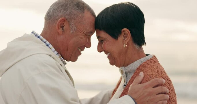 Old couple, forehead touch and hug while at beach, happiness and retirement together, travel and outdoor. Communication, happy people and pension with holiday, marriage and commitment with sunset