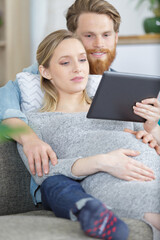 pregnant couple relaxing on the sofa looking at tablet